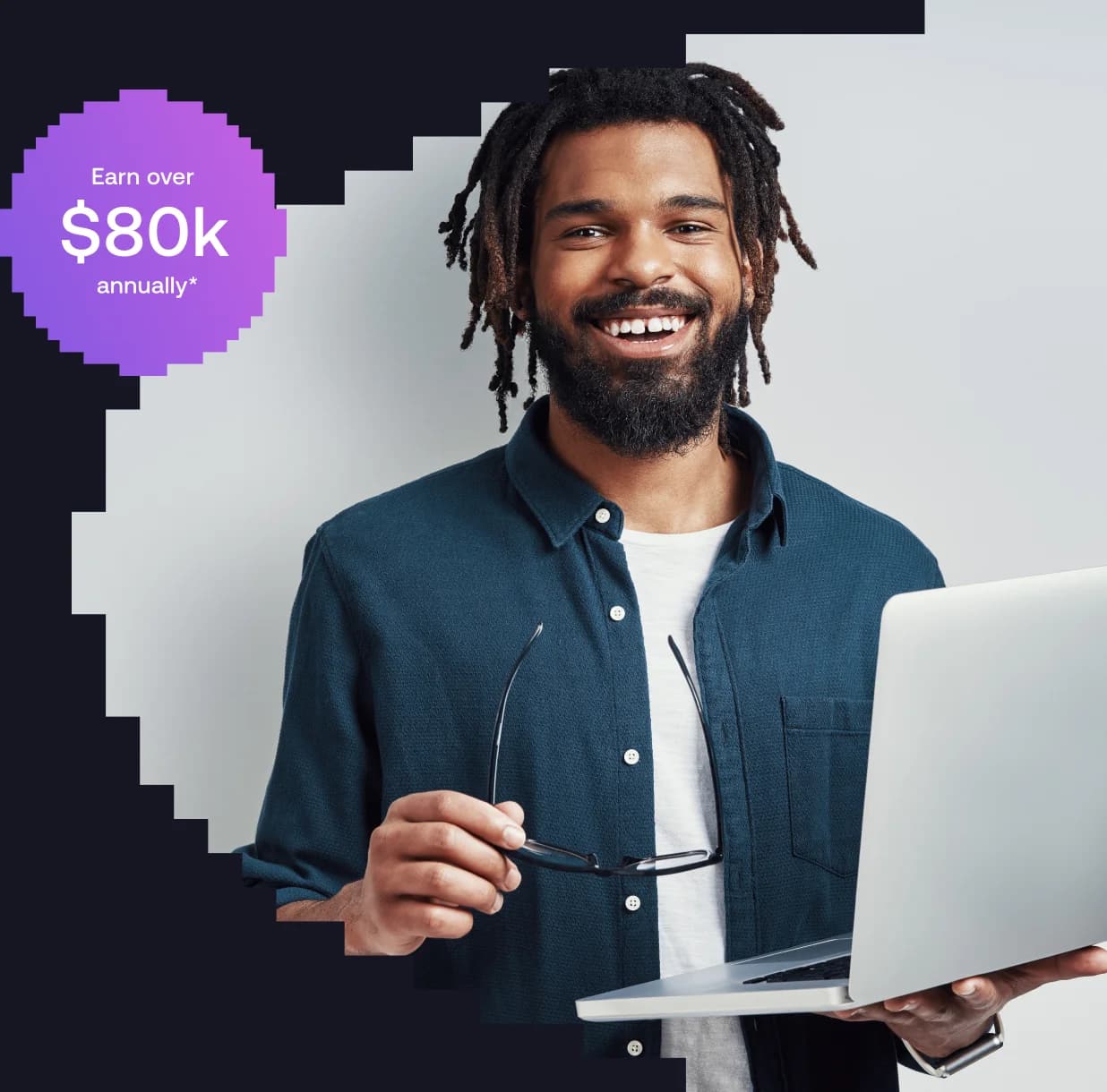 Smiling man with dreadlocks holding glasses and a laptop, wearing a dark shirt over a white t-shirt.